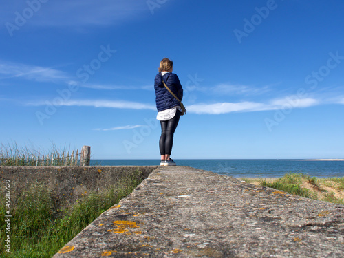 Standing woman is facing away from the camera looking at the sea beach