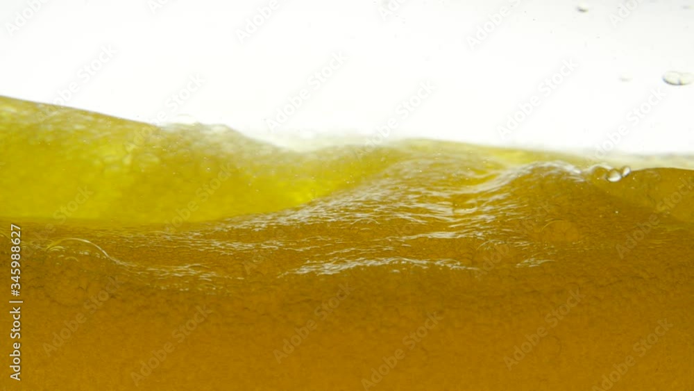 Golden liquid with bubbles on a white background, which was sharply stirred with a teaspoon. Close-up view of beer liquid in a glass bowl. Close-up view of bio fuel shot in a research laboratory. Golden liquid with bubbles on a white background, which was sharply stirred with a teaspoon. Close-up view of beer liquid in a glass bowl. Close-up view of bio fuel shot in a research laboratory.