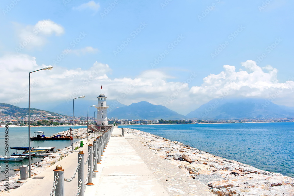 Obraz premium white beautiful lighthouse on a sea pier on a blue sky background on a sunny day