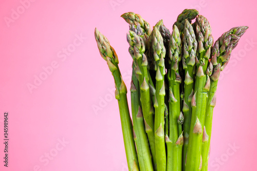 a bunch of stems of green young raw asparagus on a pink background. green low calorie vegetable rich in vitamins and folic acid