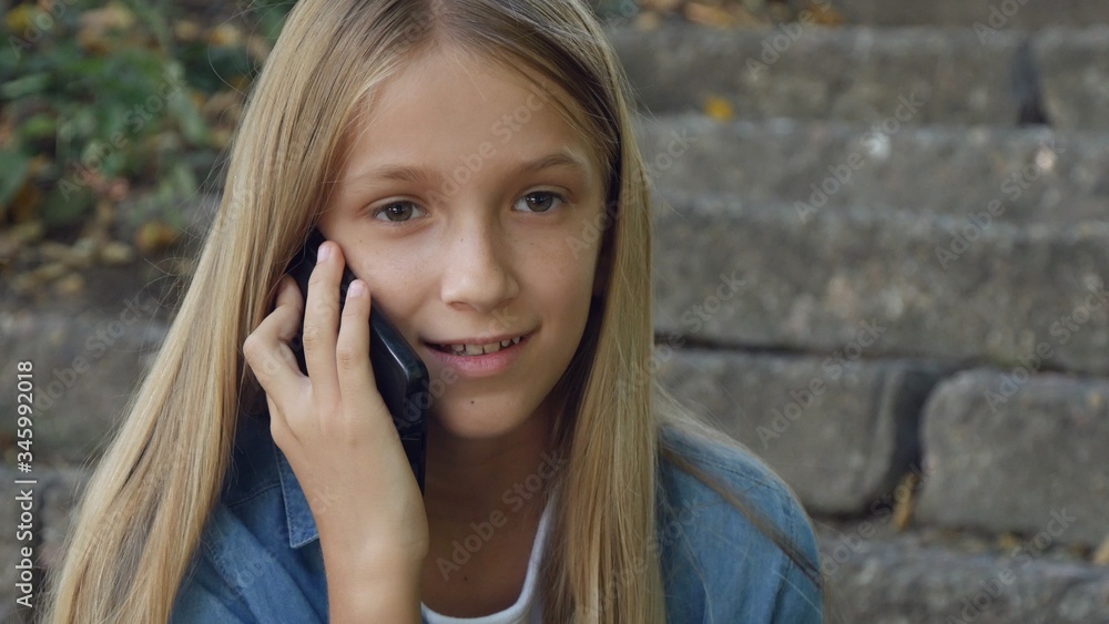 Kid Talking on Smartphone, Child Using Smart Phone, Teenager Girl Playing Outdoor in Park Kid Talking on Smartphone, Child Using Smart Phone, Teenager Girl Playing Outdoor in Park