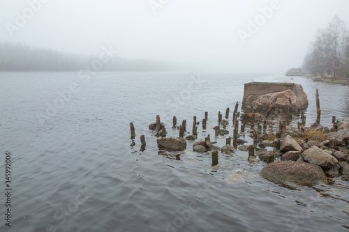 Weir by the stony lake coast in the cold misty early morning in the north of Russia © Daria