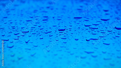Water drops on the blue surface. Beautiful colorful background with shallow depth of field. Freshness concept photo. Wide web format.
