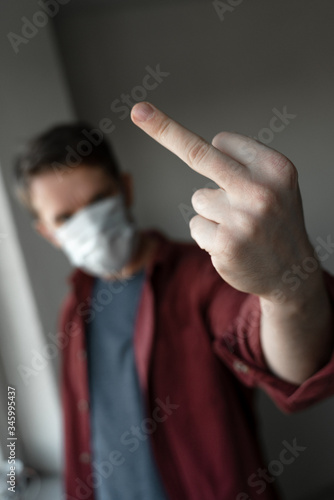 young man in medical mask shows a middle finger as a gesture in protest of quarantine and coronavirus © lusielia