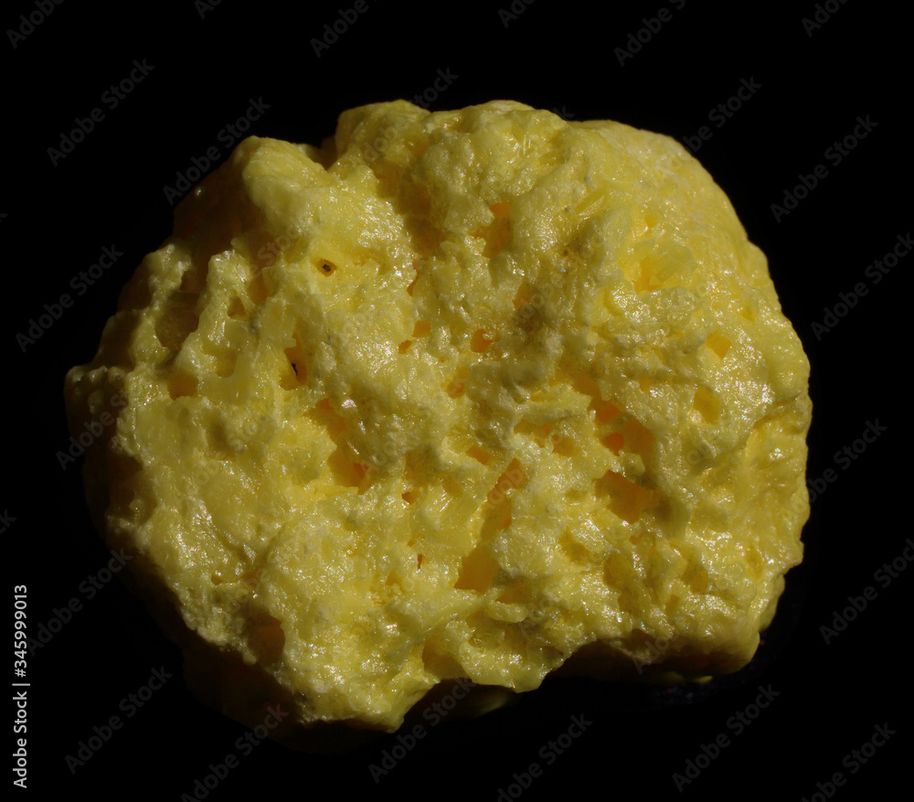 Yellow piece of native natural raw Sulfur crystal isolated on dark background. Mineral of volcanic origin Yellow piece of native natural raw Sulfur crystal isolated on dark background. Mineral of volcanic origin