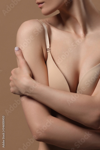 Woman hugs herself with her hands. Front view on beige background.