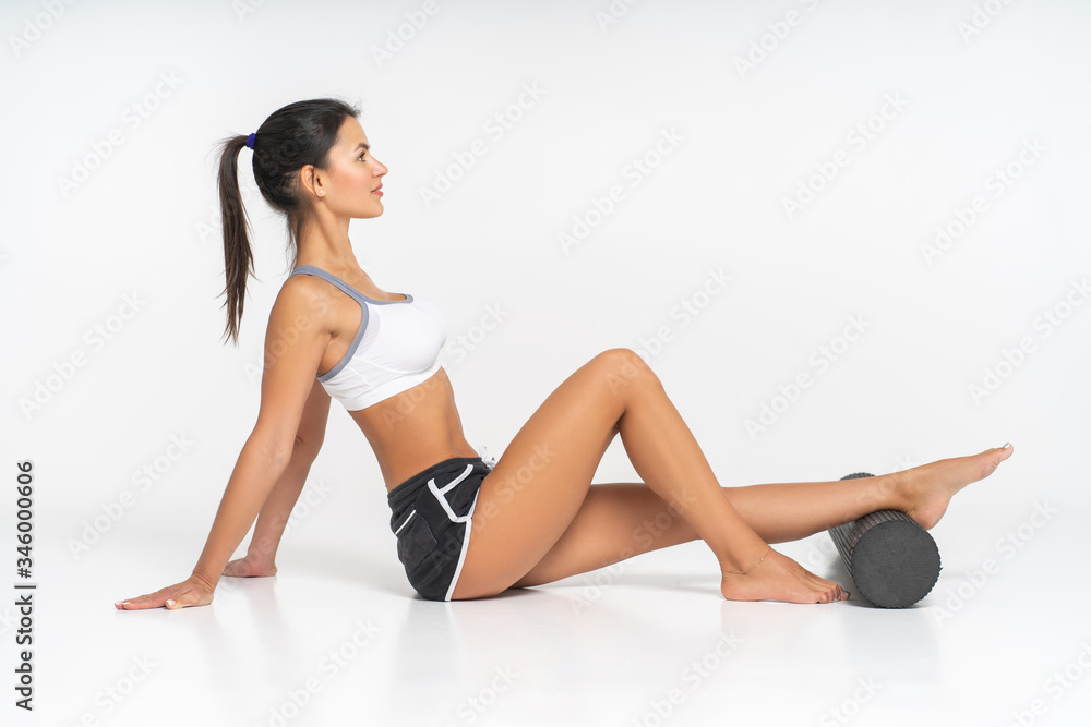 Woman rehabilitolog sitting on the floor on a white background. She has a foam roller under her feet
