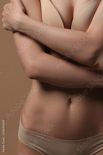 Woman hugs herself with her hands. Front view on beige background.