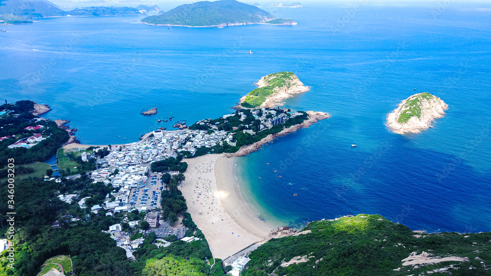 Aerial view of the Shek O Village in Hong Kong, the white sand beach with the coast line, rocky islands on blue waters, green forests on mountain's slopes. 