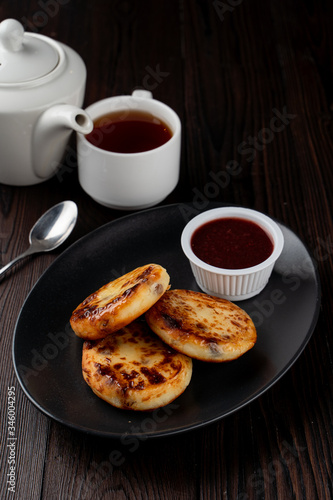 Fried russian cottage cheese patties on black plate on dark wooden table