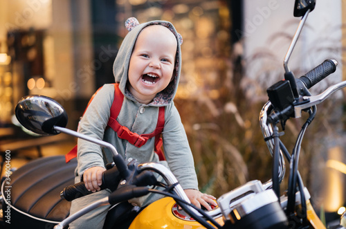 ..Small happy baby in a bodysuit sits on a motorcycle and experiences an emotion of joy. Motorcycle advertising...