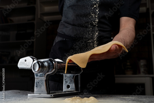 Chief is rolling raw dough in a spaghetti machine to make homemade spaghetti, only male hands visible, close up shot photo