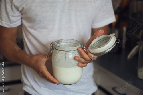 A man stands at home in the kitchen and holds a preserving jar with homemade kefir into the camera