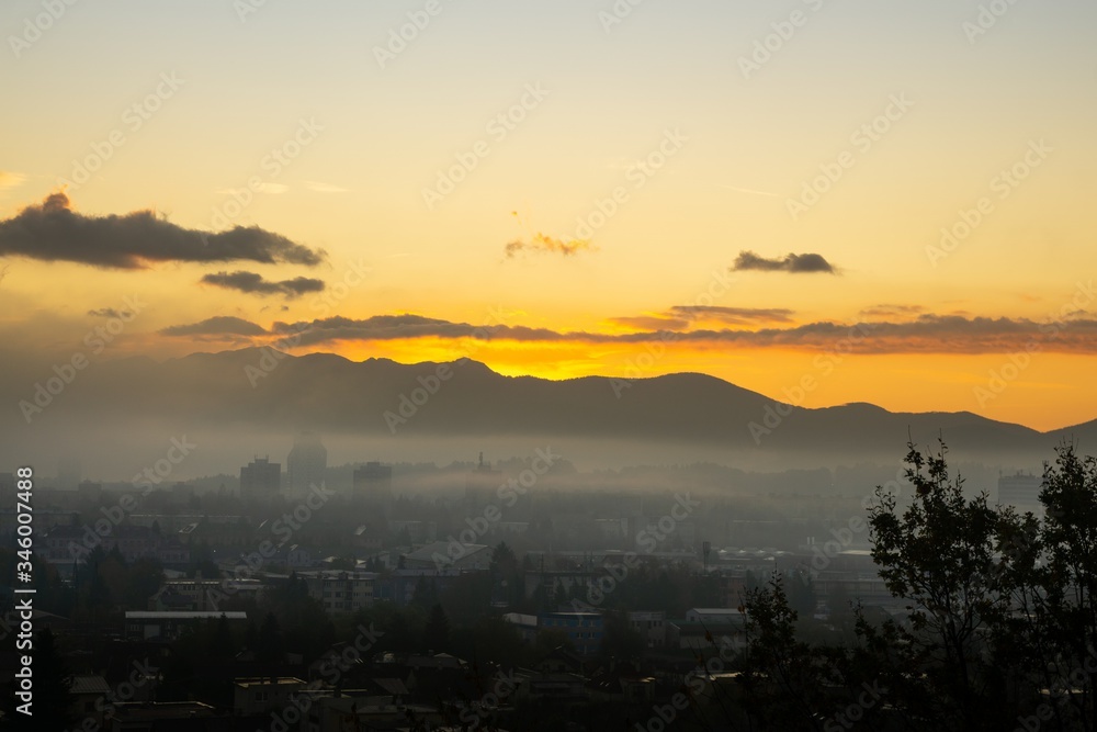 Fototapeta premium Sunrise and sunset, beautiful clouds over the meadow, hills and buildings in the town. Slovakia