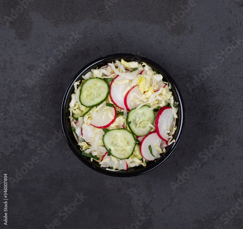 Salad of fresh cabbage, radish, cucumber and parsley on a dark background top view