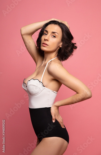 Portrait of a gorgeous trendy fit woman in swimwear while she enjoying rest with sunlight isolated over pink background. Travel, tourism, journey, trip, tour, summer concept © My Ocean studio