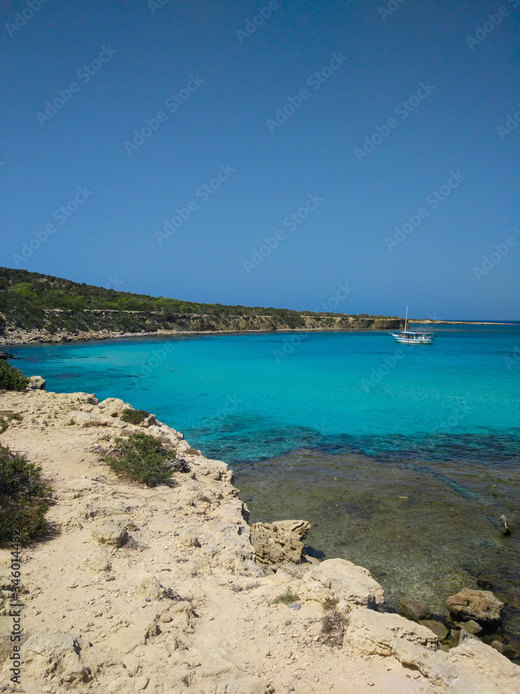 Turquoise sea with white sand and a white boat in the distance. Beautiful summer landscape.