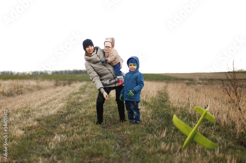 Young mother with two children, a little girl and a boy playing in the autumn field. Autumn family in the Park playing with toy airplane.