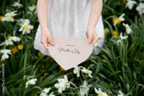Happy Mother's Day written on a paper card held by a girl on a flower and grass background