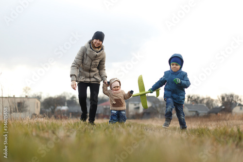 Young mother with two children, a little girl and a boy playing in the autumn field. Autumn family in the Park playing with toy airplane.