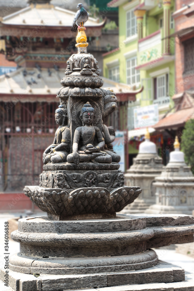 One of many stone buddhist statues of sitting Buddha in Kathmandu city, Nepal. Pigeon sits on top of monument. Religious architecture theme.