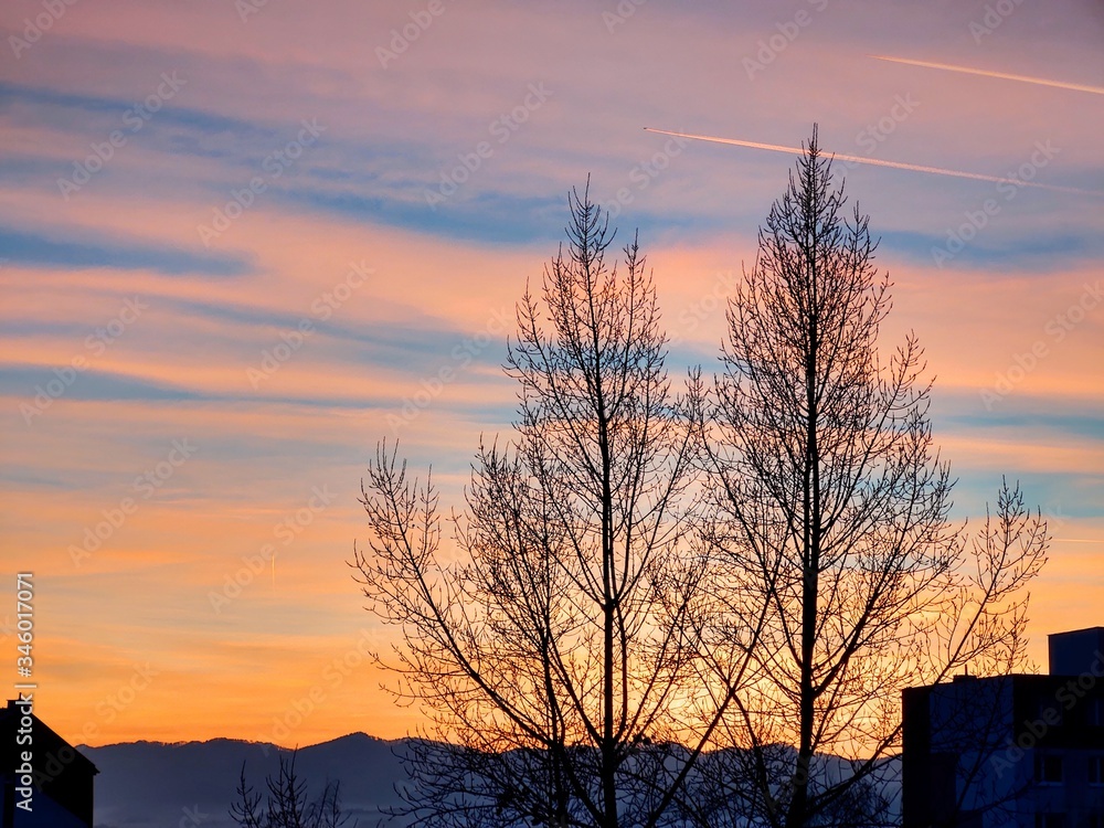 Naklejka premium Sunrise and sunset, beautiful clouds over the meadow, hills and buildings in the town. Slovakia