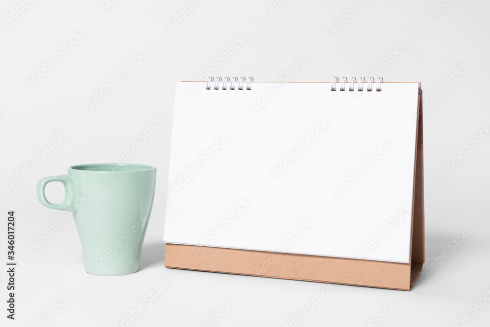 Blank paper spiral calendar for mockup template advertising and branding with cup on gray background. Blank paper spiral calendar for mockup template advertising and branding with cup on gray background.