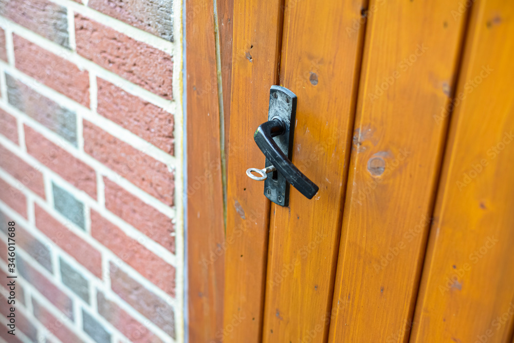 Closed wooden garden door with key inside with black handle, visible red brick wall. Closed wooden garden door with key inside with black handle, visible red brick wall.