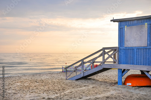 Beautiful sunset over the calm sea on a cloudy hot summer evening. Visible wooden lifeguard house in blue. © Michal