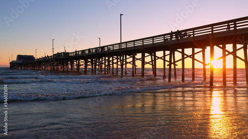 People walking on the Newport Beach pier during sunset as waves slowly roll in to the beach. © Stock Footage, Inc.