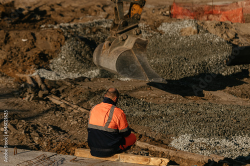 A worker sits at a construction site. Work on the excavator.