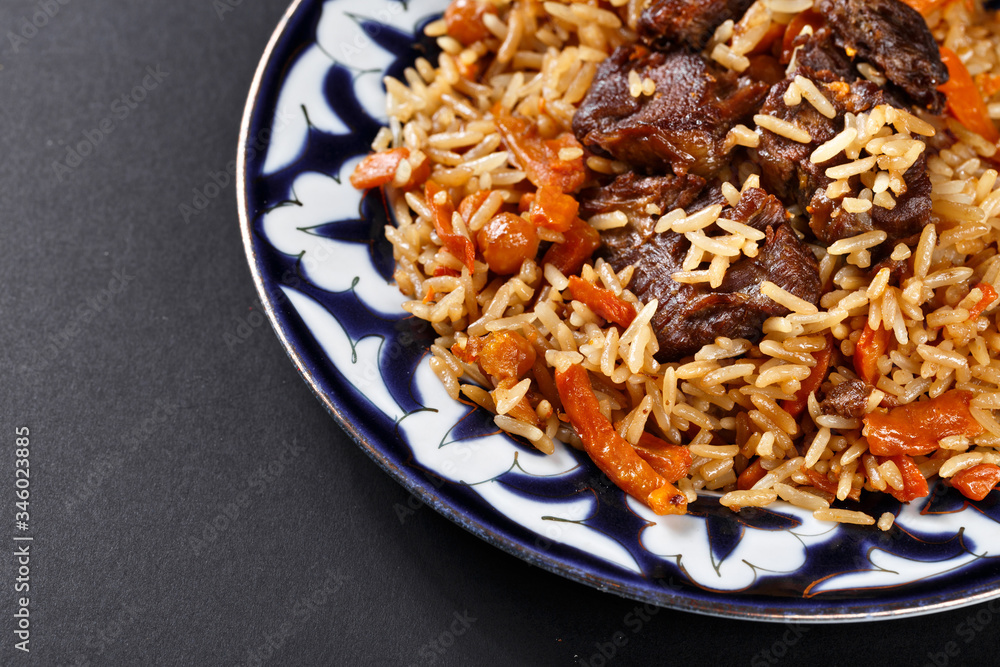 Plov pilaf plate on black background. Traditional Uzbek cuisine.