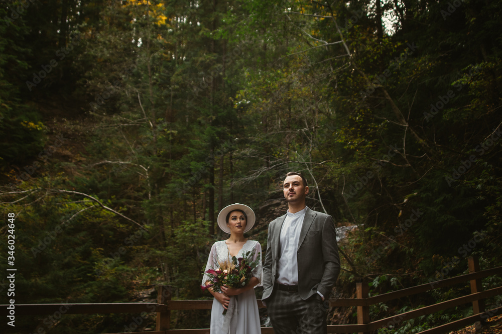 the groom stands in front of the bride against the backdrop of a mountain forest the groom stands in front of the bride against the backdrop of a mountain forest