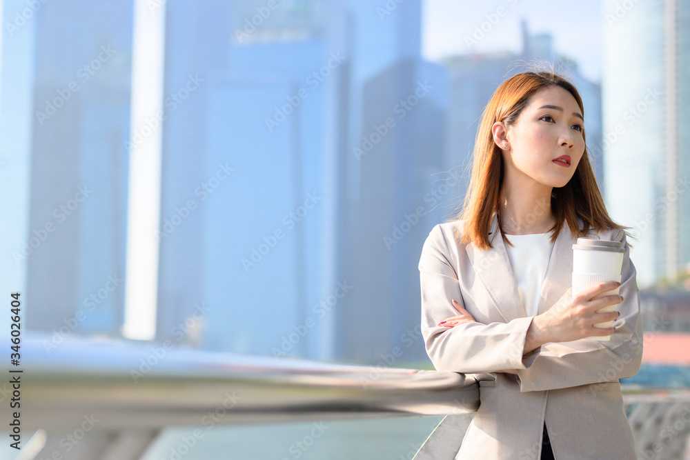Business person, Coffee break and using phone concept, Young Asian woman holding portable-coffee mug and using smart phone while coffee break in urban city