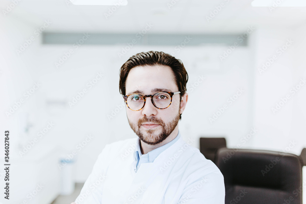 Handsome male doctor with bristles in glasses and a white coat in a light medical office. Handsome male doctor with bristles in glasses and a white coat in a light medical office.