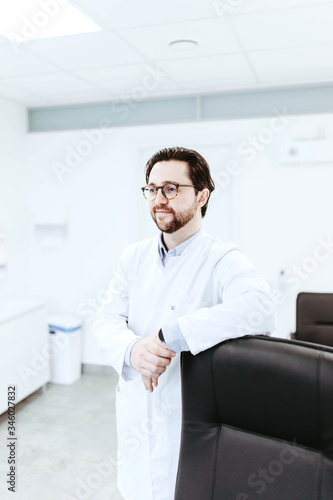 Portrait of a young male doctor in a white coat in a medical office. specialist in glasses with bristles. © velimir