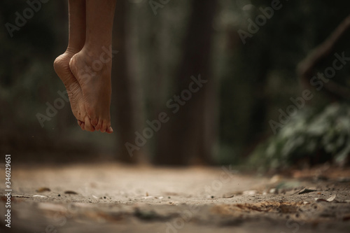 Close up of two barefoot feet of a young woman, floating in midair in the middle of a park. Making the dust spread.