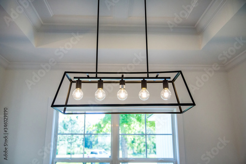 Hanging retro black metal iron chandelier lighting fixture with vintage bulbs hanging in a dining room of a new construction house