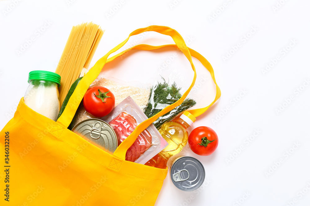 Set of grocery items from vegetables, canned food, pasta, oil, cereal in yellow eco shopping bag on white background. Top view.