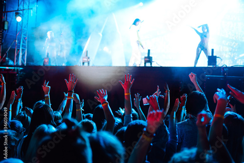Сrowd with raised hands at music festival. Fans enjoying rock concert with light show and clapping hands.