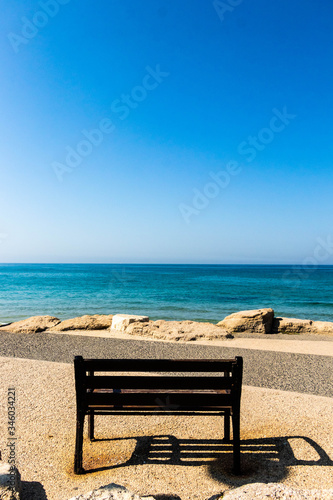 lonely bench by the sandy sunny beach against the backdrop of the turquoise sea