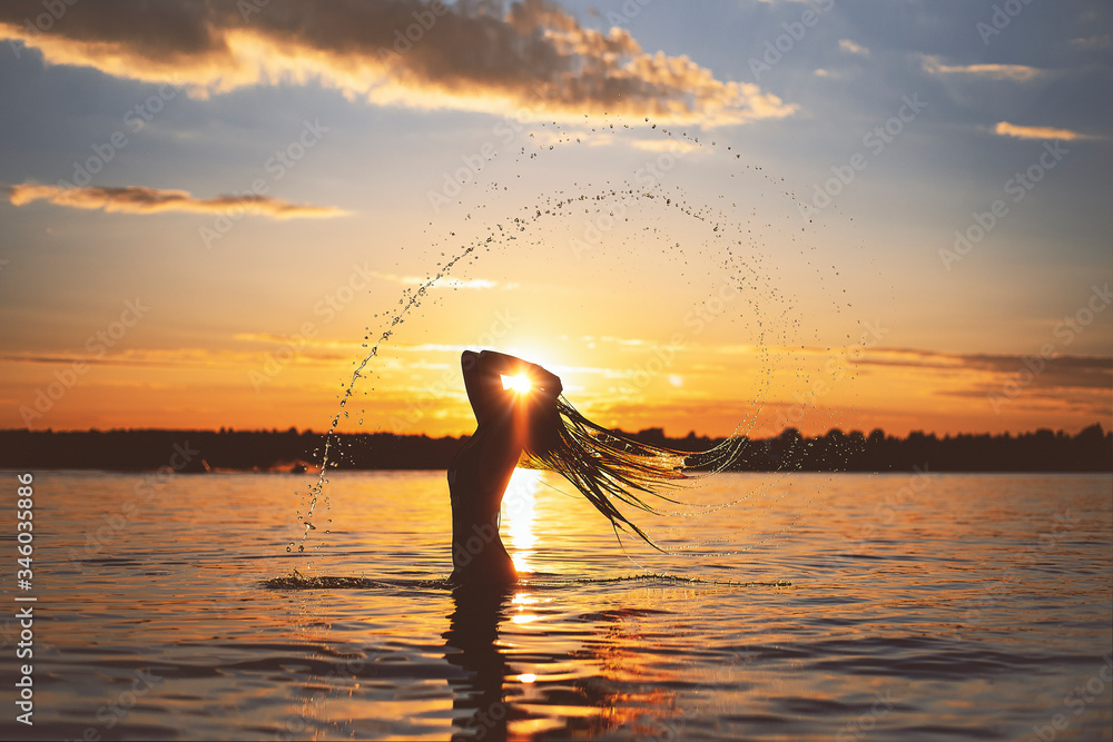 girl with long hair on the beach in the water at sunset