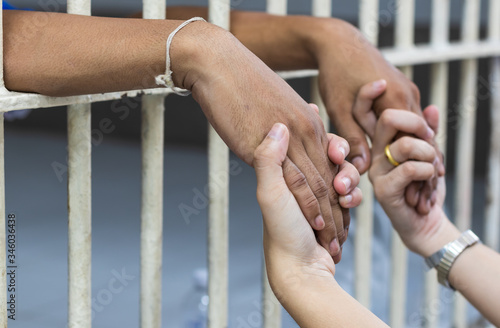 Fotografering Woman holding the hand of a male prisoner in a white cage.