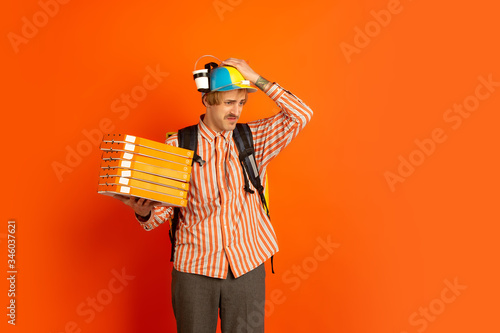 Sad, tired holding pizza boxes. Emotions of caucasian deliveryman isolated on orange background. Contacless delivery service during quarantine. Man delivers food during isolation. Safety. Hurrying up. photo