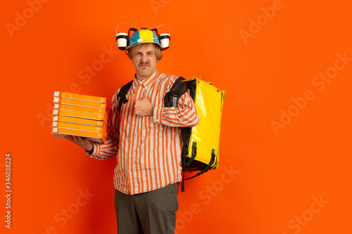 Sad, angry holding pizza boxes. Emotions of caucasian deliveryman isolated on orange background. Contacless delivery service during quarantine. Man delivers food during isolation. Safety. Hurrying up. photo