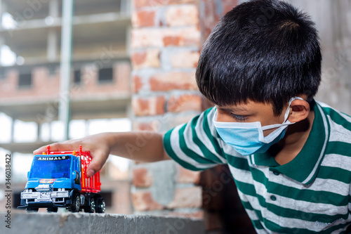 A boy is playing with toy cars in their own home. He using a facial mask made of ordinary cloth fabrics for safety purposes. He is quarantined at home. photo