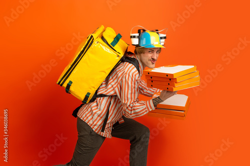 Fast and fun getting. Emotions of caucasian deliveryman isolated on orange background. Contacless delivery service during quarantine. Man delivers food during isolation. Safety. Hurrying up. photo