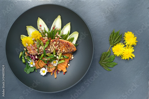 Wild herbs salad with grilled salmon, carrot, wild garlic buds, roasted sunflower seeds,chicory, young maple leaves and chopped radicchio. Garnished with edible wild flowers, dandelion and daisy.