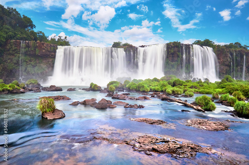 Iguazu waterfalls in Argentina. Panoramic view of many majestic powerful water cascades with mist. Panoramic image with reflection of blue sky with clouds. © tilialucida