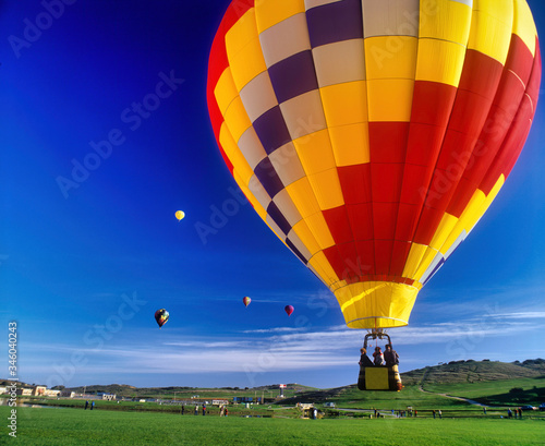 Colorful hot air balloon taking off over a striking green field.
